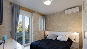 Una camera da letto con parete in pietra, un letto con biancheria scura, un comodino con una lampada e una finestra con tende.