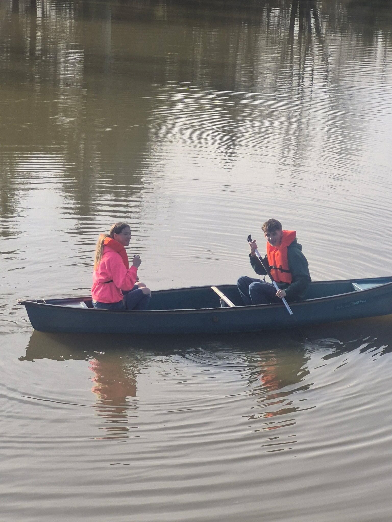 Un petit bateau, avec deux personnes à bord, l’une portant une veste rose et l’autre une veste foncée, naviguant sur une eau calme.