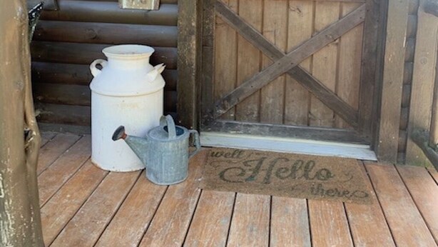 A rustic cabin entrance with a wooden door, a lantern, a sign reading "CABIN", a white pot, a watering can, and a "Hello there" mat. - Big Mike's Cabin on the lake, next to ball diamonds nestled in 3 -cabin village (Hamersville)