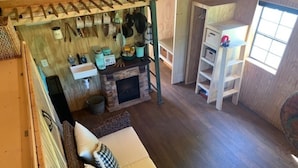A rustic interior with a stone fireplace, wooden shelves, and a hanging rack with kitchen utensils. - Big Mike's Cabin on the lake, next to ball diamonds nestled in 3 -cabin village (Hamersville)