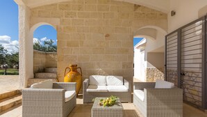 Un área de patio al aire libre con muebles de mimbre, un jarrón grande y una pared de piedra.