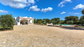 Un patio empedrado con un edificio blanco, una entrada arqueada y una zona de piscina al fondo.