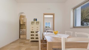 Un comedor con una mesa de madera, sillas blancas y un mueble blanco con cajones.