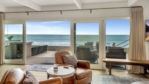 A spacious room with a large sliding glass door leading to a balcony with ocean views. There is a leather sofa, a small round table, and a bench. - ON THE SAND!! Private Beach! OCEAN FRONT HOT TUB!! STR14-0126 (Dana Point)