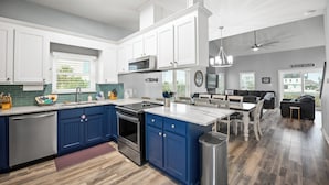 A modern kitchen with white and blue cabinetry, a central island, and a dining area with a ceiling fan.