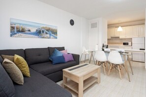 A modern living room with a sofa, a coffee table, and a dining area with chairs and a kitchen in the background.