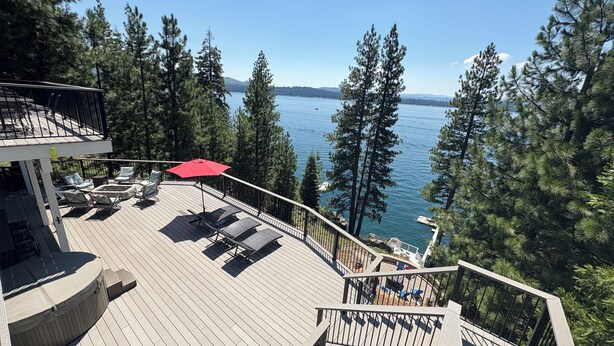 A deck with lounge chairs and a red umbrella overlooking a lake surrounded by trees.