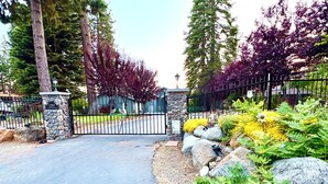 A gated driveway leading to a building with a stone pillar and a sign reading 'Lifesaver Water.'