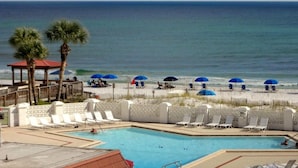 A pool area with lounge chairs and umbrellas, a beach with people, and a clear view of the ocean. - El Matador 316 by AJH Rentals FREE BEACH SERVICE+ACTIVITIES! $300/Day (Fort Walton Beach)