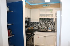 Una cocina con armarios blancos, encimera negra, salpicadero de azulejos y fregadero de acero inoxidable.