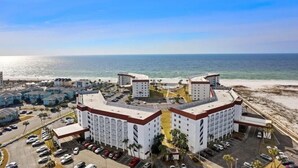 A beachfront hotel with multiple buildings, parking lots, and a view of the ocean.