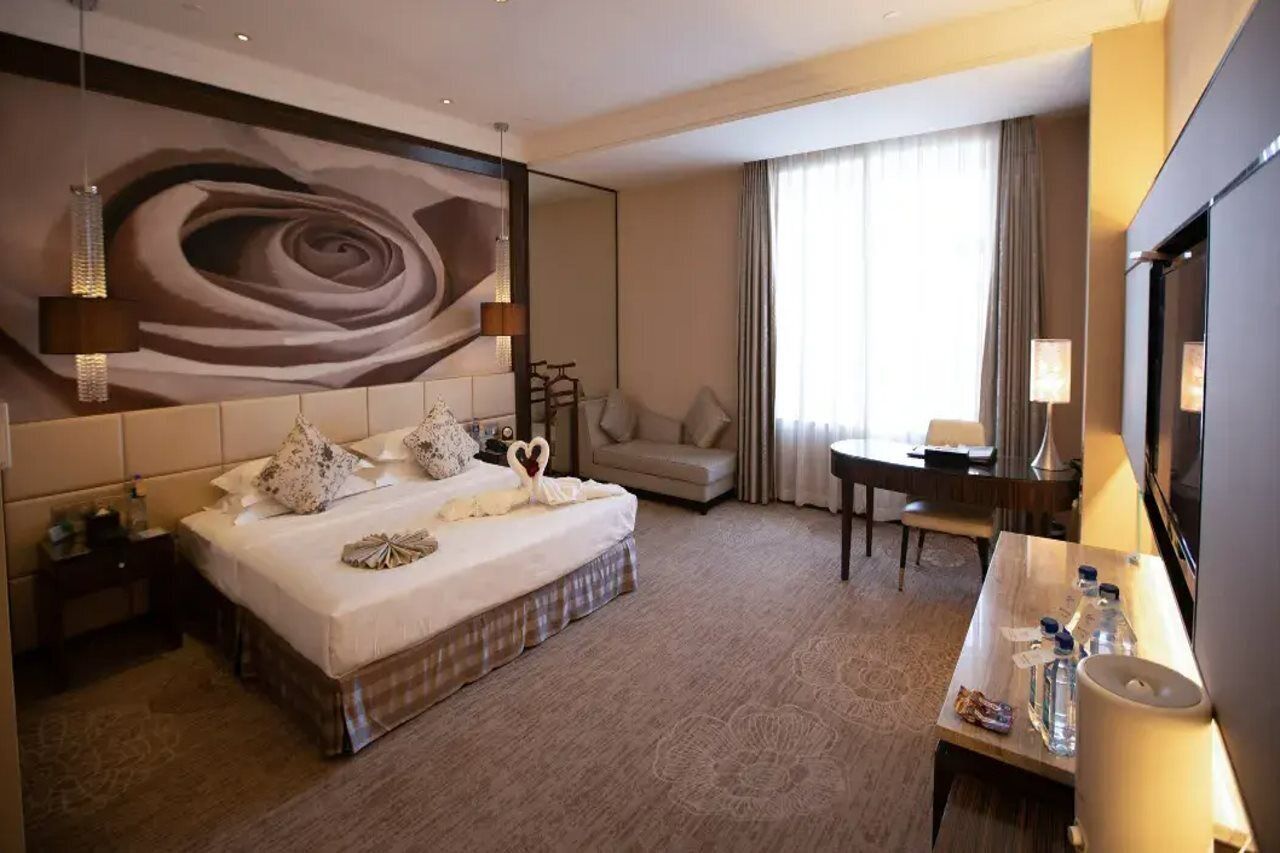 Ein Hotelzimmer mit einem großen Bett, einem Schreibtisch, einem Sessel, einem Fernseher und einem großen Spiegel.