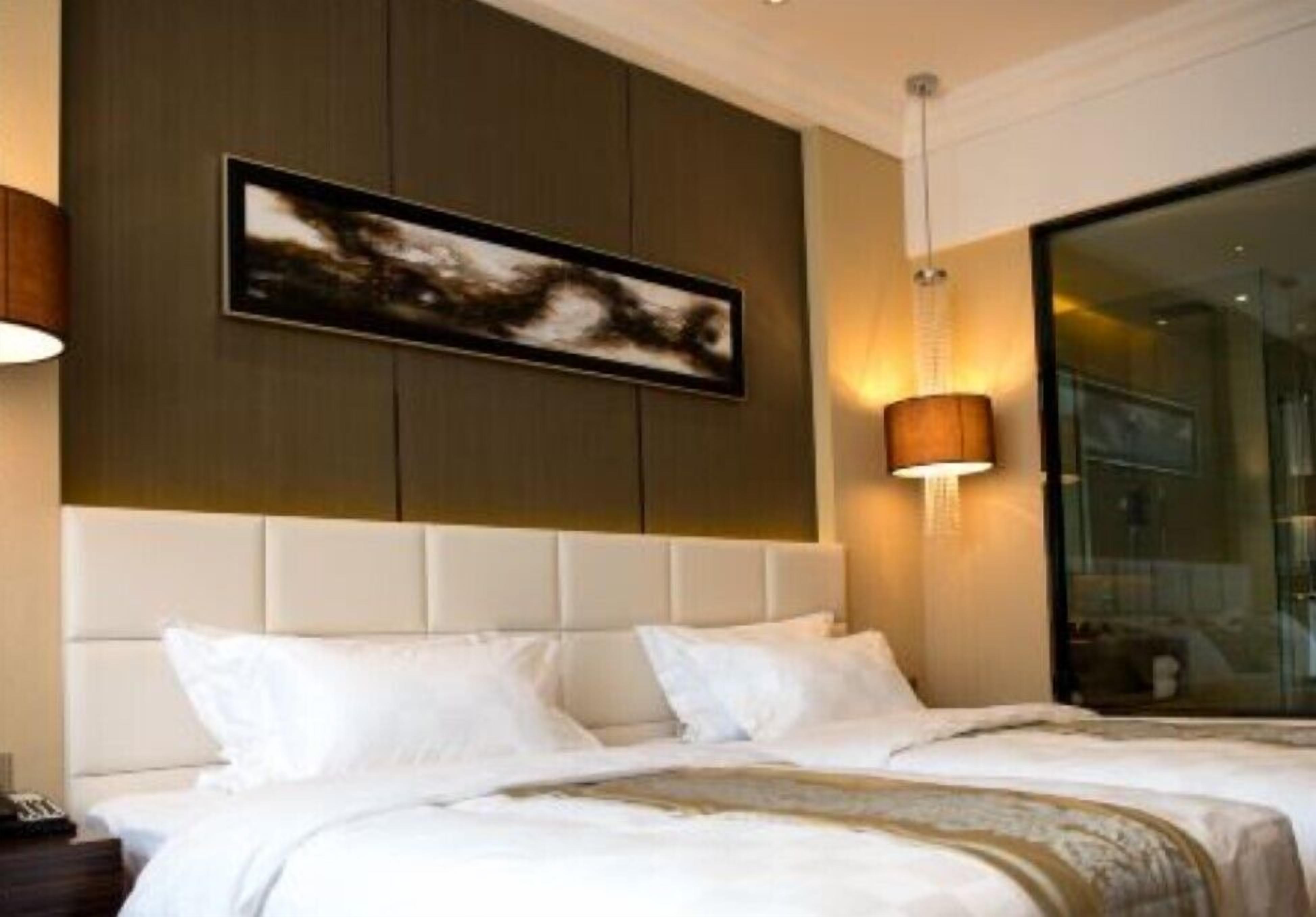 A hotel room with a large bed, a headboard, a wall-mounted artwork, and a bedside lamp.