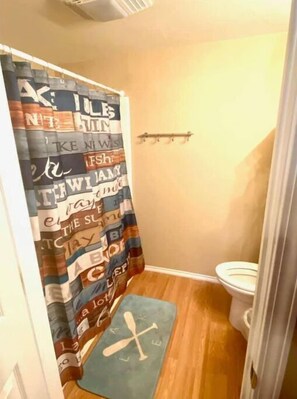 Bathroom features a shower curtain with colorful patterns, a standard toilet, and a small shelf above.