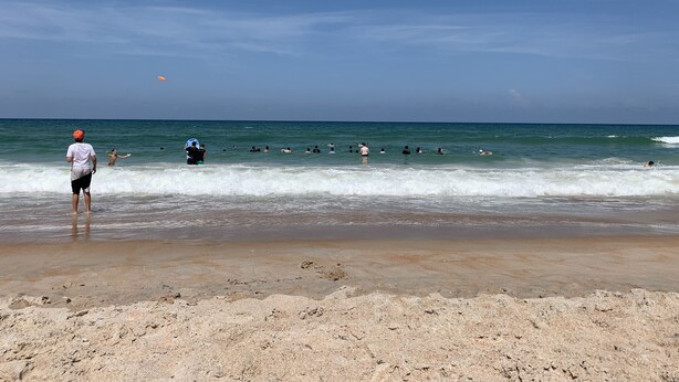 Una playa con gente nadando y jugando en el agua.