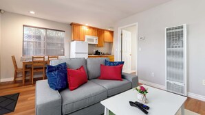 A living room with a grey sofa, red and blue pillows, a white coffee table with a remote control, and a kitchen in the background. - Bright, Quiet, Comfy 1BR Cottage in Mountain View (Mountain View)