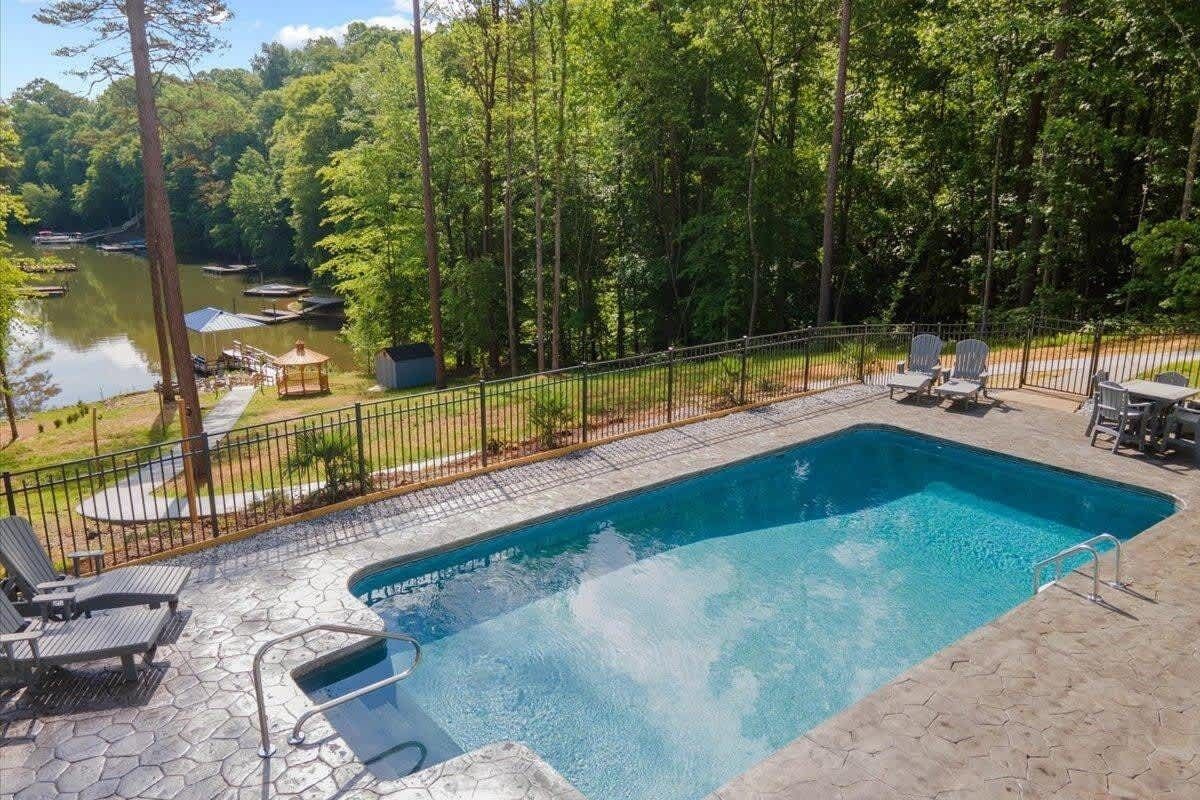 A rectangular swimming pool with a metal fence, surrounded by lounge chairs and a gazebo.