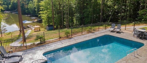 A rectangular swimming pool with a metal fence, surrounded by lounge chairs and a gazebo.