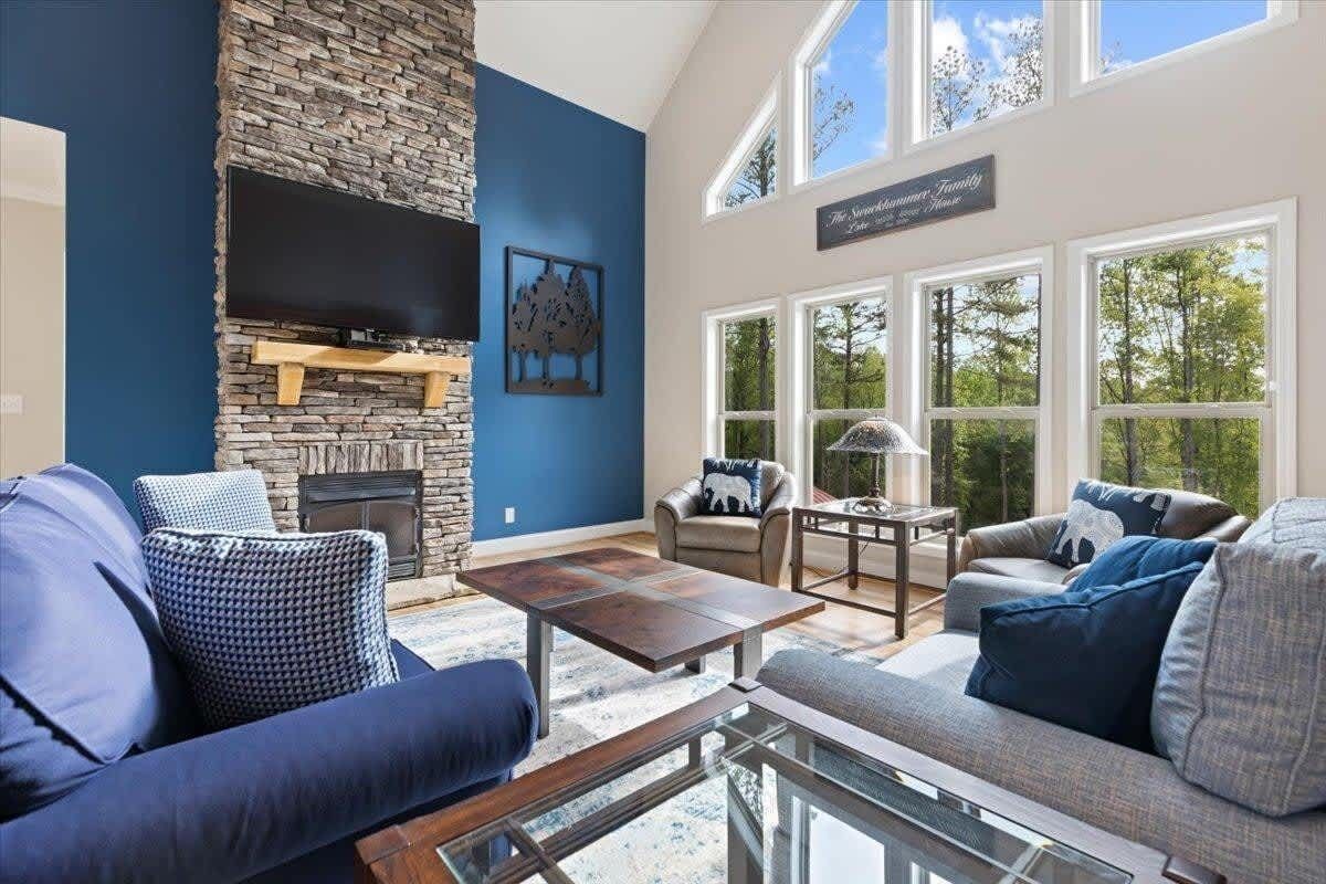 A living room with a stone fireplace, blue walls, and large windows.