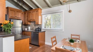 A kitchen with wooden cabinets, a stainless steel refrigerator, a dishwasher, and a dining area with a wooden table and chairs. - Spacious, Soaring Ceilings, Near Downtown MV, GOOG (Mountain View)