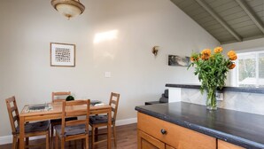 A dining area with a wooden table and chairs, a vase with flowers on the counter, and a painting on the wall. - Spacious, Soaring Ceilings, Near Downtown MV, GOOG (Mountain View)