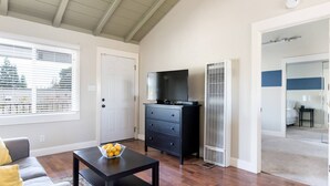 A modern living room with a sofa, a coffee table with a fruit bowl, a black TV stand, and a white air conditioning unit. - Spacious, Soaring Ceilings, Near Downtown MV, GOOG (Mountain View)