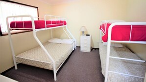 Ein Zimmer mit zwei Etagenbetten, einem kleinen weißen Nachttisch, einem Deckenventilator und einem Fenster mit Jalousien.