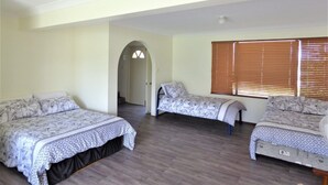 A room with three beds, a wooden floor, a window with blinds, and an arched doorway. - Bear's a well located fisherman and family holiday home in Harrington (Harrington)