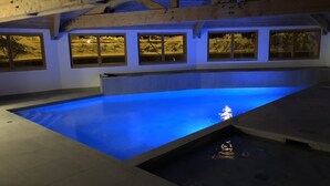 En inomhuspool med blått upplysta kanter, träbjälkar och fönster med utsikt över ett snötäckt landskap.