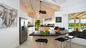 A modern kitchen with a central island, bar stools, a ceiling fan, and a view of a pool. - Sol e Luna (3 bedrooms) - Beautiful villa with pool, Terres Basses, St. Martin (Terres Basses)