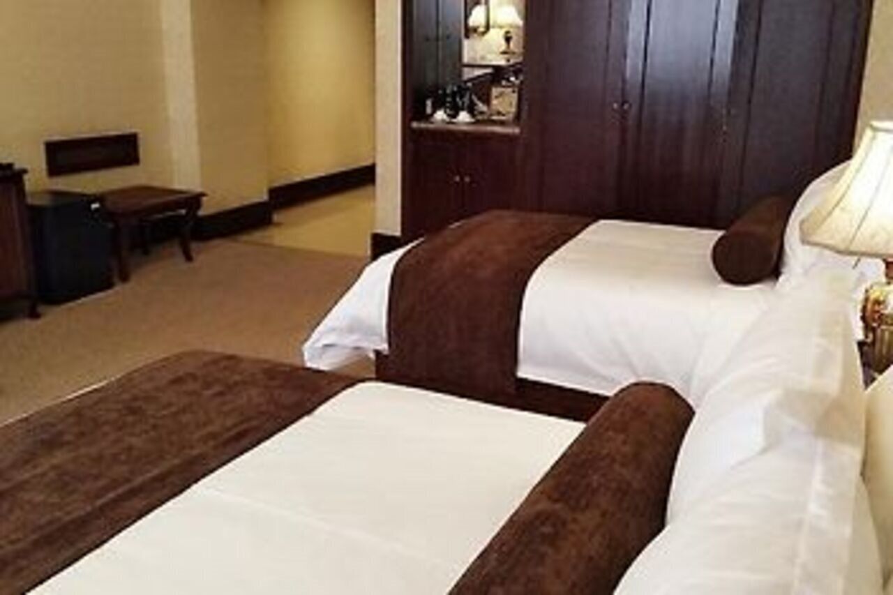 Quarto de hotel com duas camas, uma escrivaninha, uma cadeira e uma mesa de cabeceira com abajur.