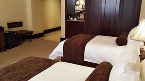 Una habitación de hotel con dos camas, un escritorio, una silla y una mesita de noche con lámpara.
