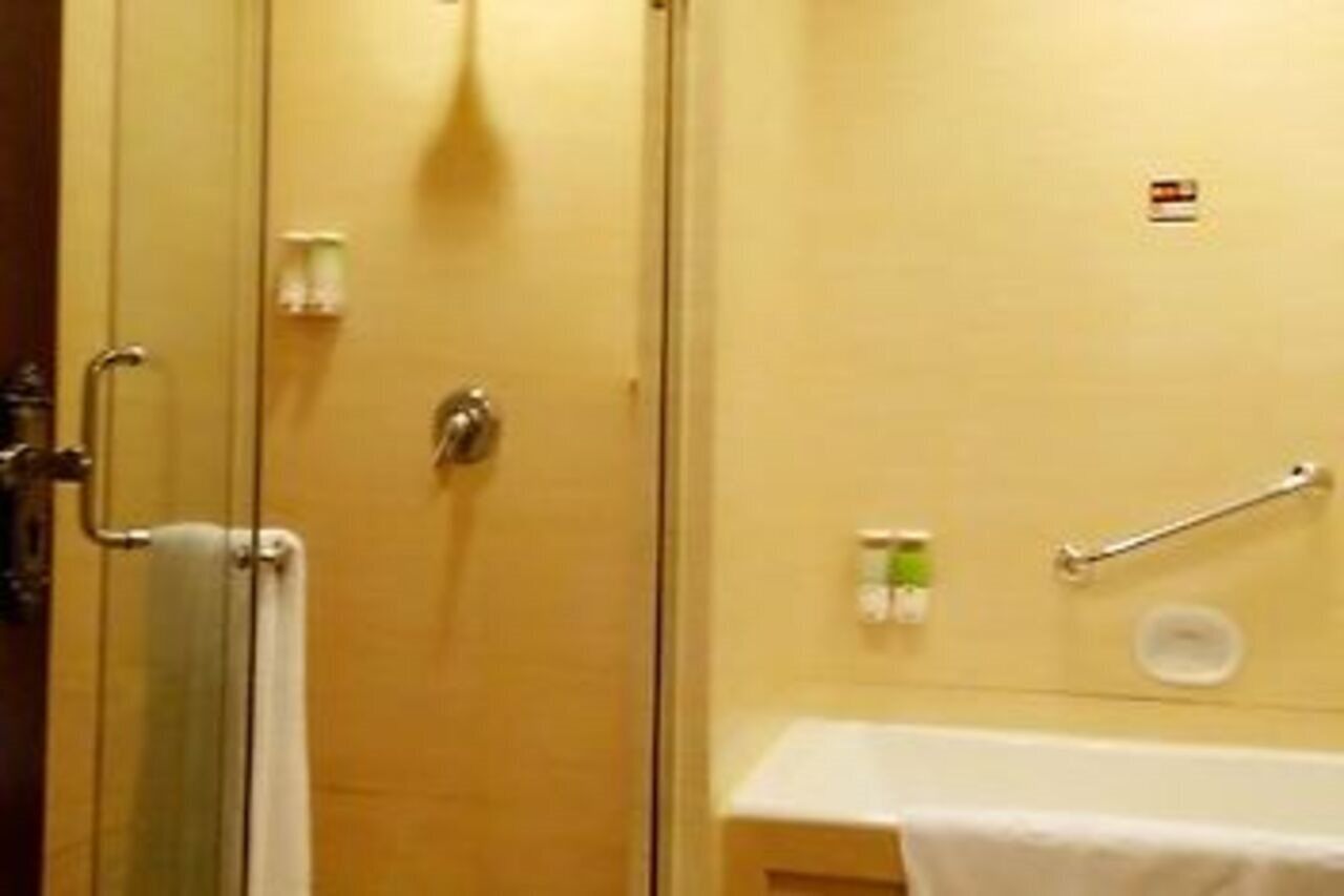 A bathroom with a glass shower door, a towel rack, a handrail, and a small sink.