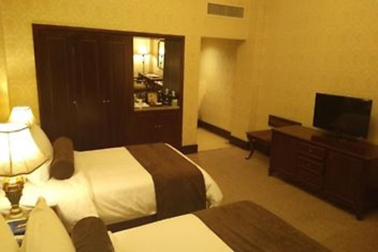 Una habitación de hotel con dos camas, un aparador, un televisor y un espejo.