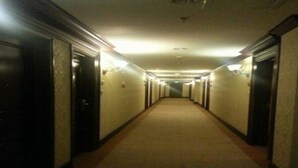Un pasillo largo y estrecho con piso alfombrado y paredes, con puertas a ambos lados e iluminación en el techo.