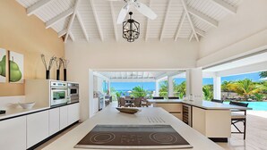 Une cuisine moderne dotée d’un îlot central, d’un four encastré et offrant une vue sur la piscine et l’océan.