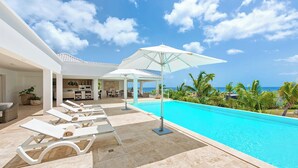 Un espace aménagé au bord de la piscine, avec des chaises longues, un coin salon abrité et une vue sur l’océan.