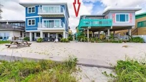 A beachfront property with a two-story building, a covered patio, and a sandy beach area.