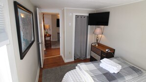 Une chambre à coucher avec un lit, un bureau, une télévision et une salle de bain visible à travers une porte ouverte.