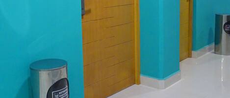 Un pasillo con paredes color turquesa, una puerta de madera con el número 202 y un bote de basura con la etiqueta 'extinto'.
