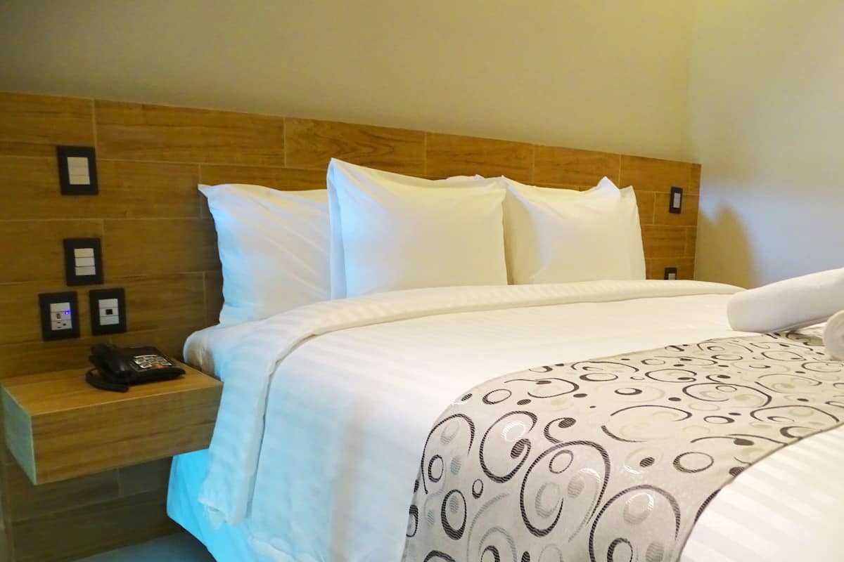 Une chambre d’hôtel avec un lit bien fait, une tête de lit en bois, une table de chevet avec un téléphone et un interrupteur fixé au mur.