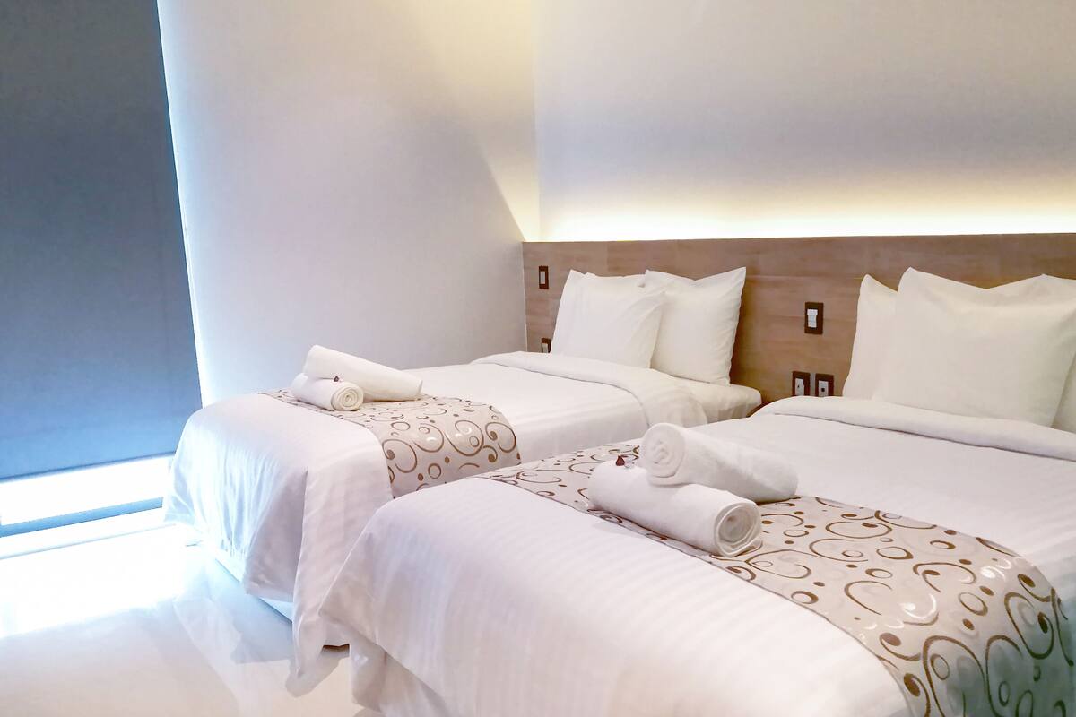 Une chambre d’hôtel avec deux lits, chacun agrémenté de draps blancs et de coussins décoratifs.