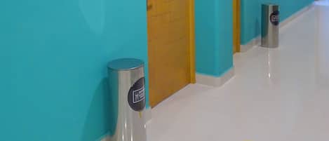Un pasillo con paredes verde azulado, puertas de madera y un suelo con un letrero amarillo de distanciamiento social.