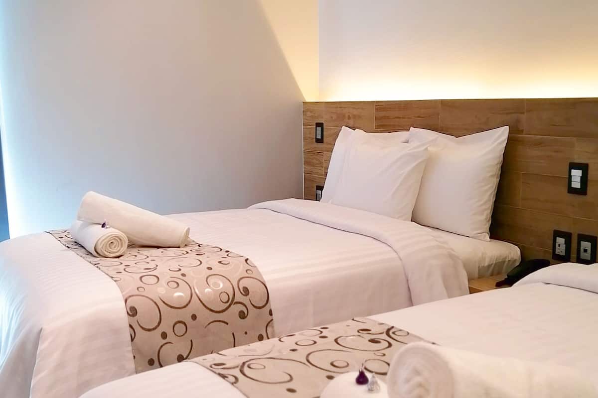 Une chambre d’hôtel avec deux lits, chacun doté d’une tête de lit, de draps blancs et d’un couvre-lit à motifs.