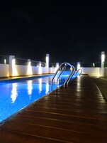 Una piscina con barandillas de metal y un muelle de madera de noche.