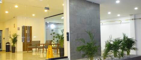 A hotel entrance with a glass facade, a reception desk, and a staircase leading to the lobby.