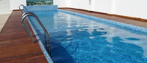 A rooftop swimming pool with a wooden deck and glass railings.