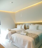 Una habitación de hotel moderna con dos camas, un cabecero de madera y una lámpara en el techo.