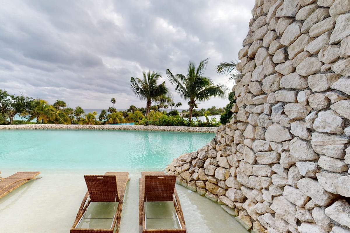 Un área junto a la piscina con sillones de descanso y un muro de piedra.