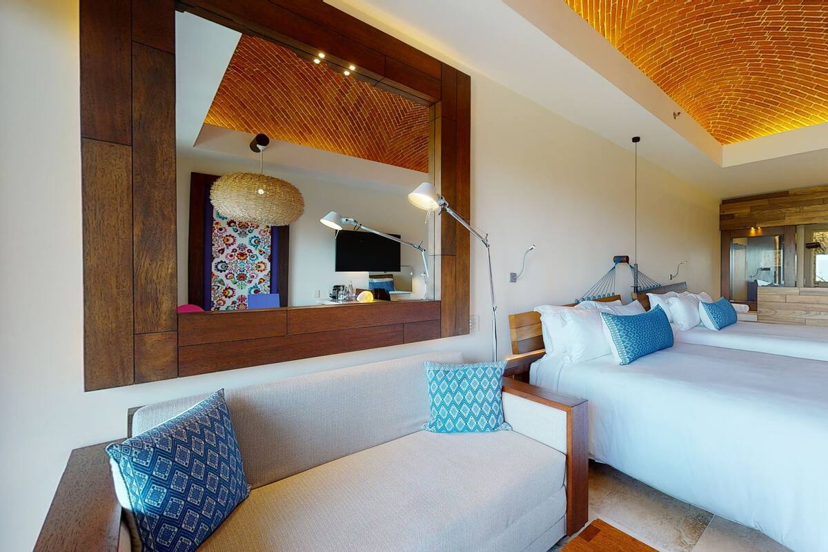 Una habitación de hotel moderna con dos camas, un espejo grande, un sofá y un techo con diseño de ladrillo.